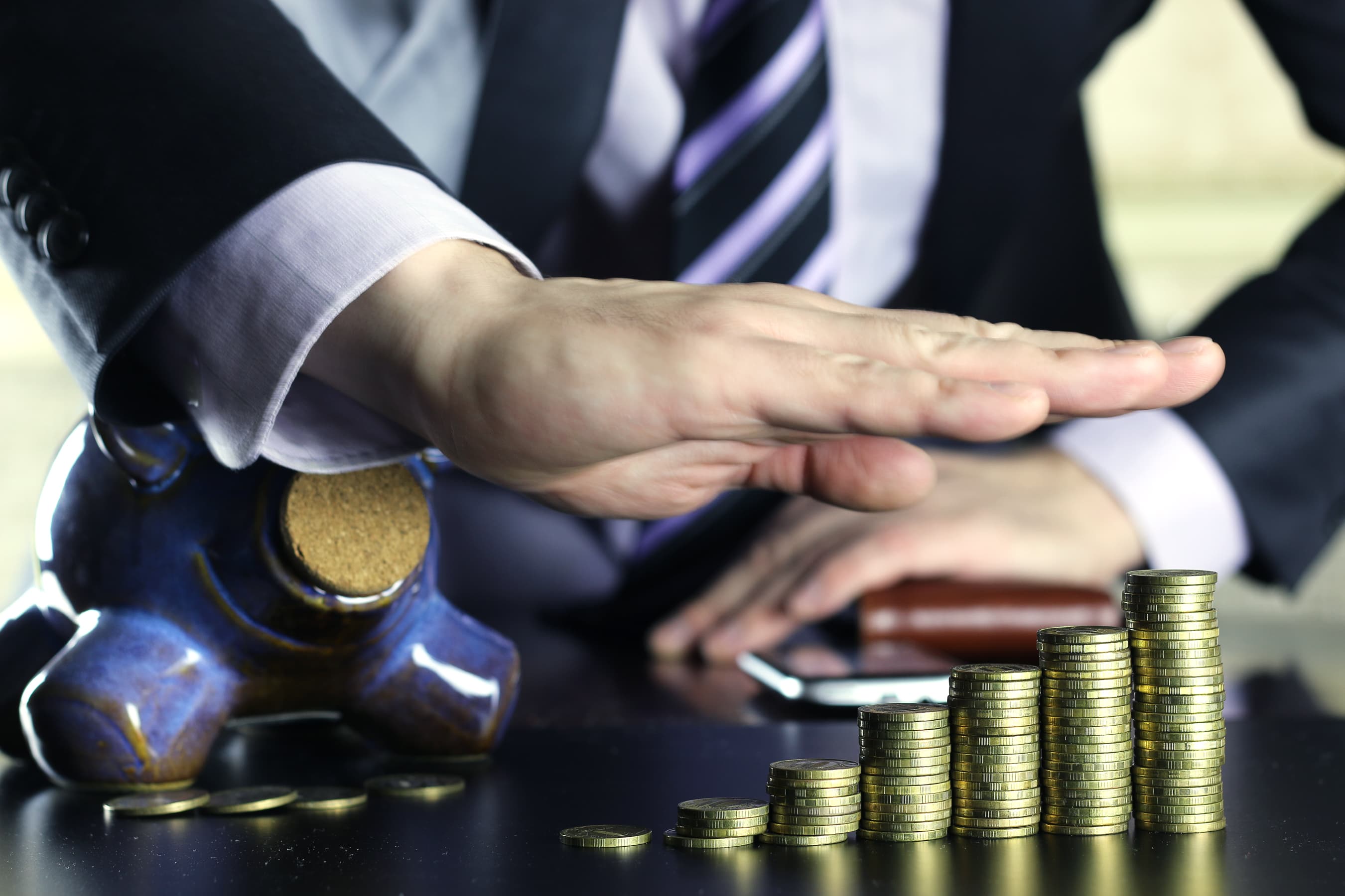 A businessman's hand beside a piggy bank and rising stacks of coins