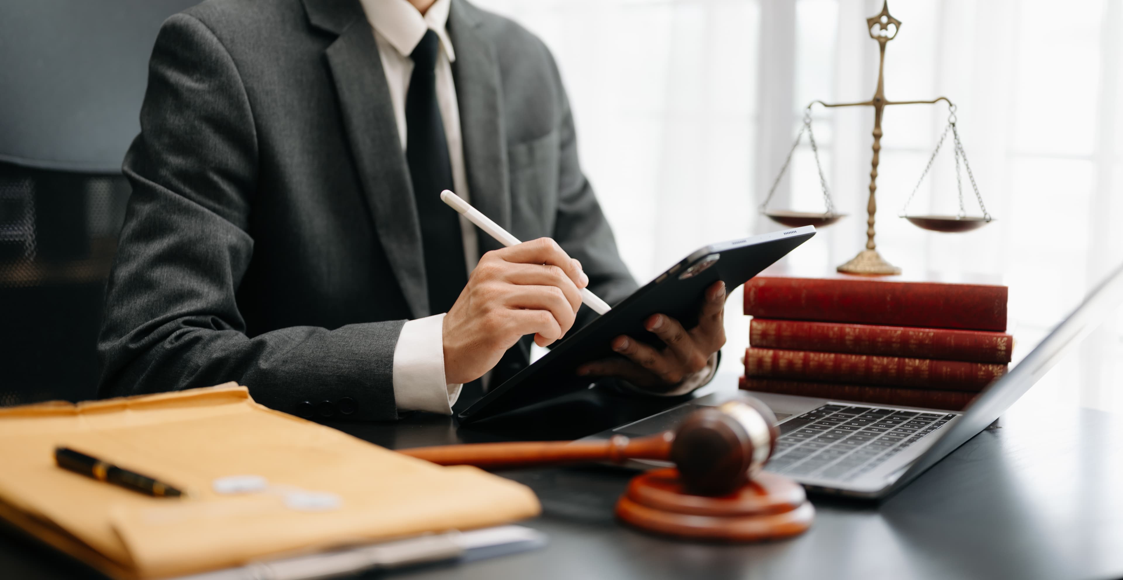 A lawyer reviewing case documents on a tablet beside the scales of justice and a gavel