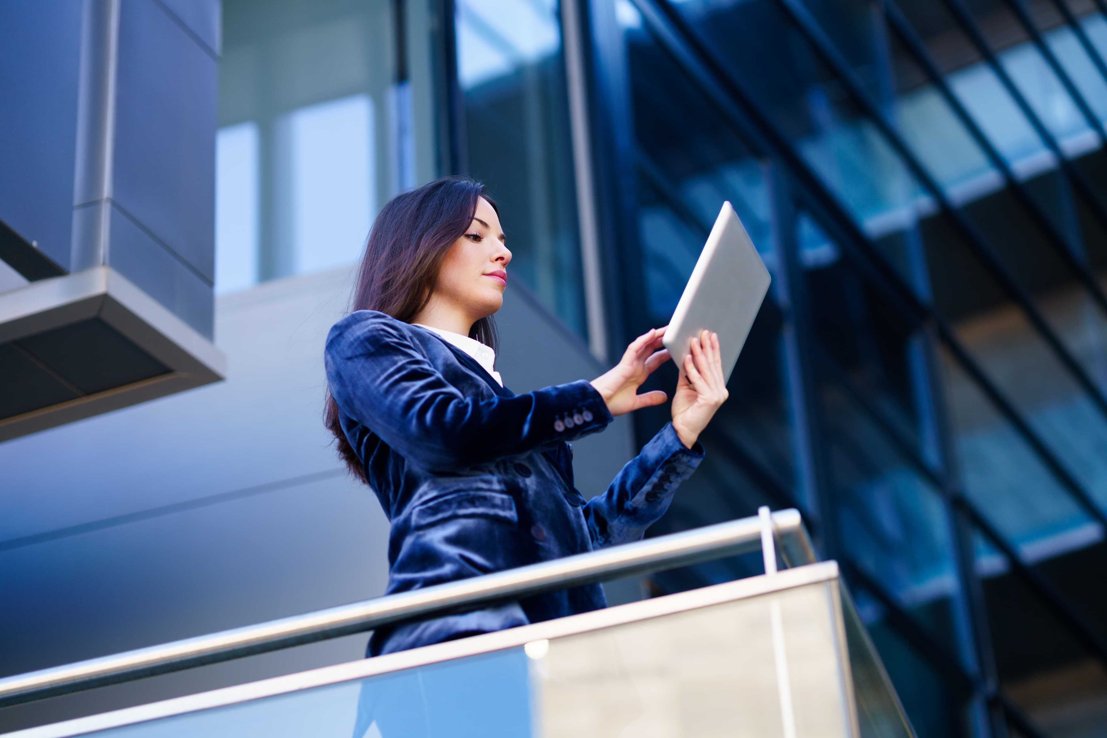 A business professional reviewing compliance documents on a tablet outside a modern office building